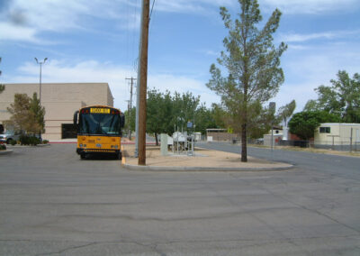 A yellow school bus is parked near a curb in an empty parking lot with trees and a building visible in the background.