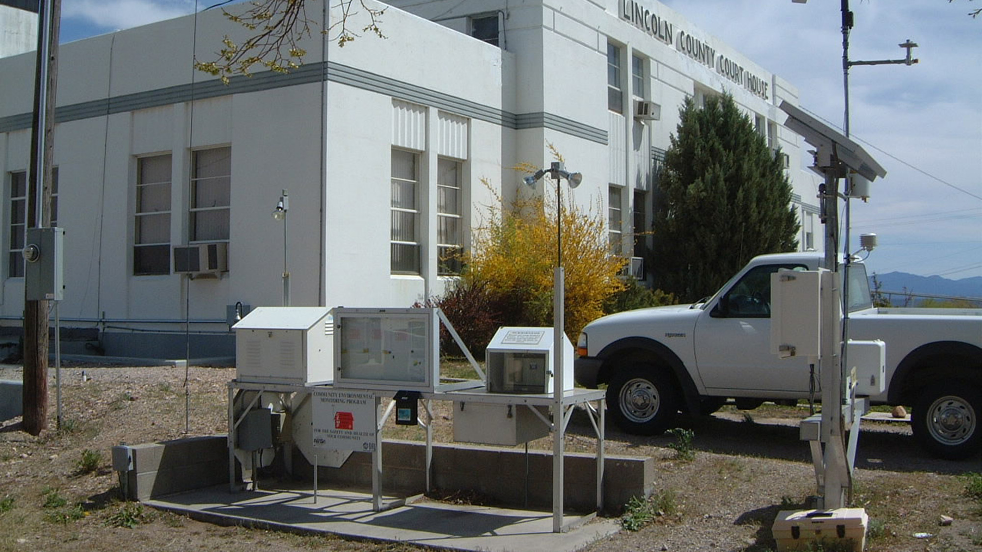 A white building with weather monitoring equipment in the foreground and a white pickup truck parked nearby.